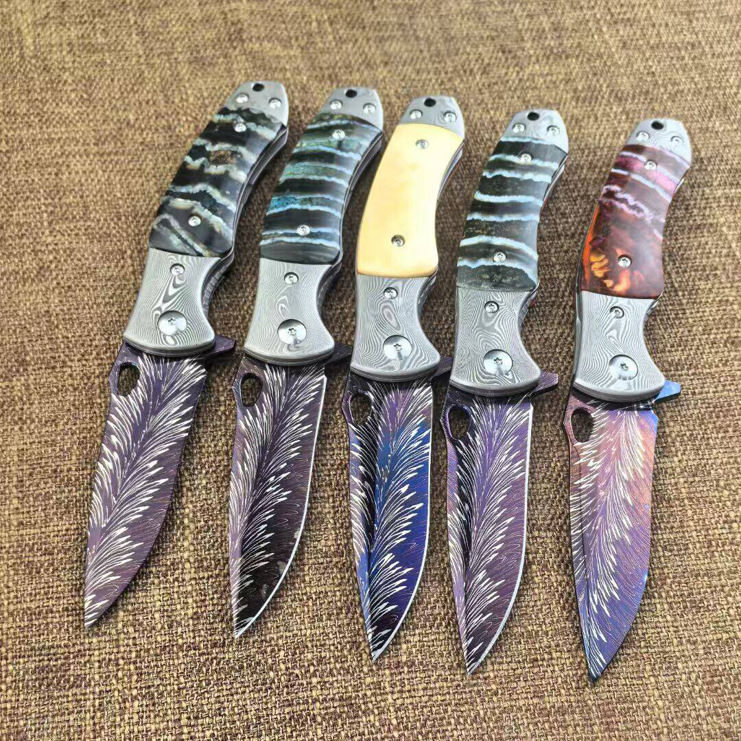 ​​Five forged folding knives with blued steel blades featuring gold wire feather engravings and mammoth ivory/composite handles on brown fabric background