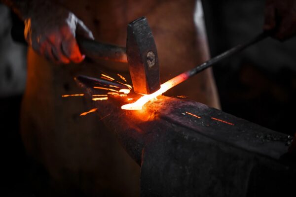 Artisan blacksmith hammering glowing red blade blank on anvil with flying sparks - Traditional knife forging scene